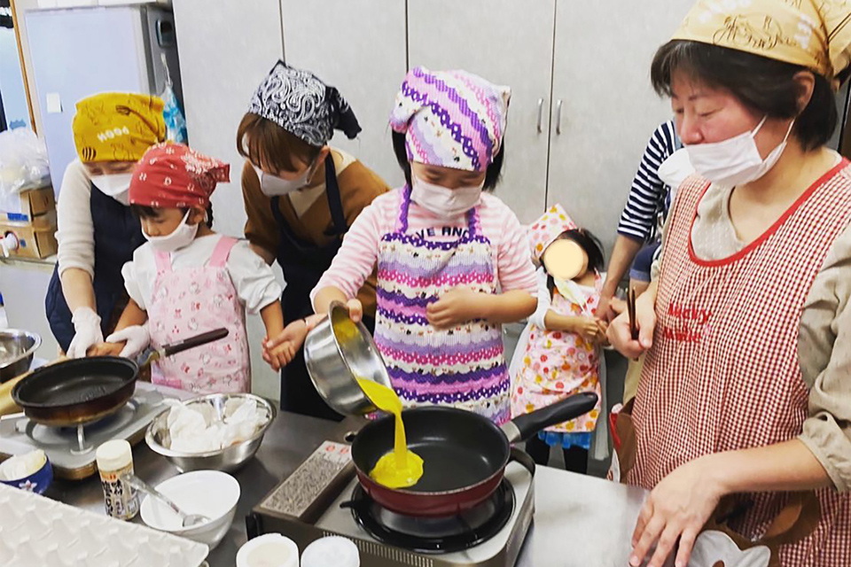 子どもがフライパンで卵を焼く様子を見守る井村ユリエさん（右）